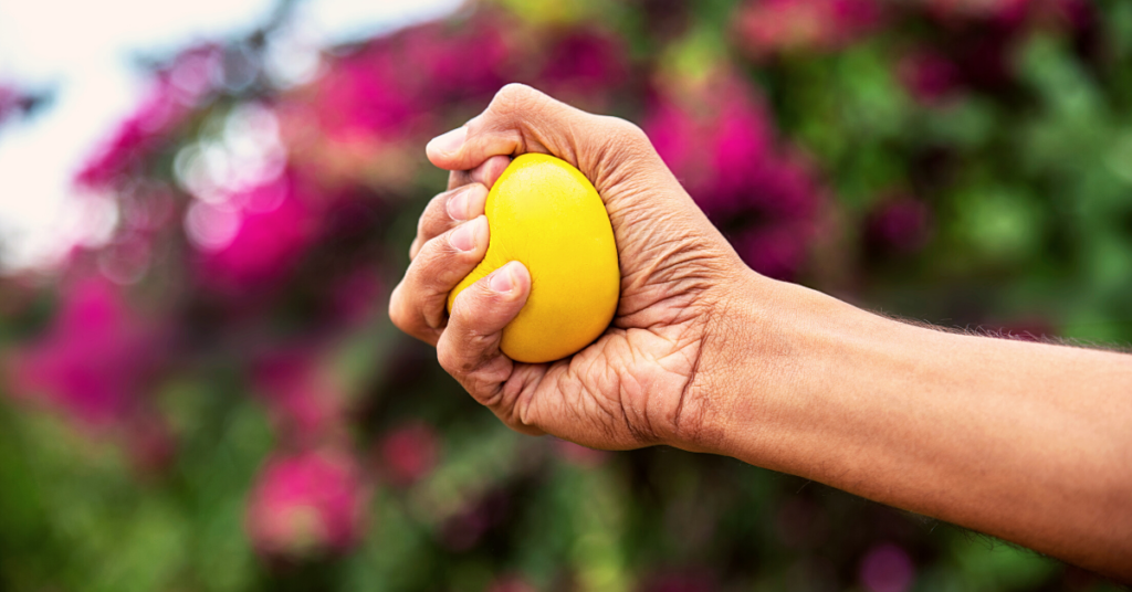 hand with yellow stress ball in front of flowering bush