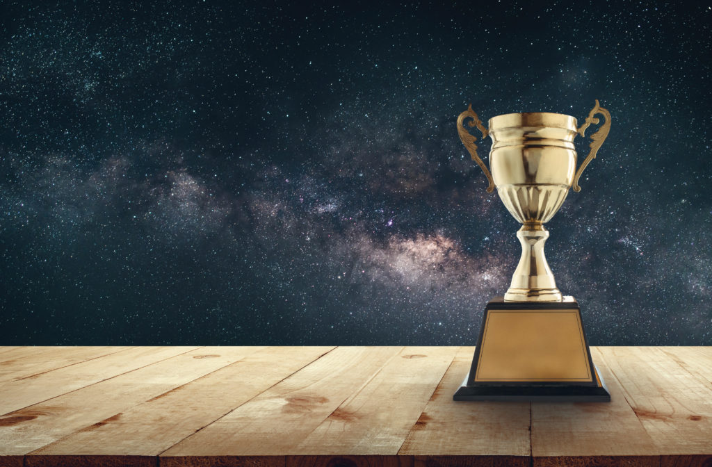 gold trophy on wooden surface in front of cosmic blue sky